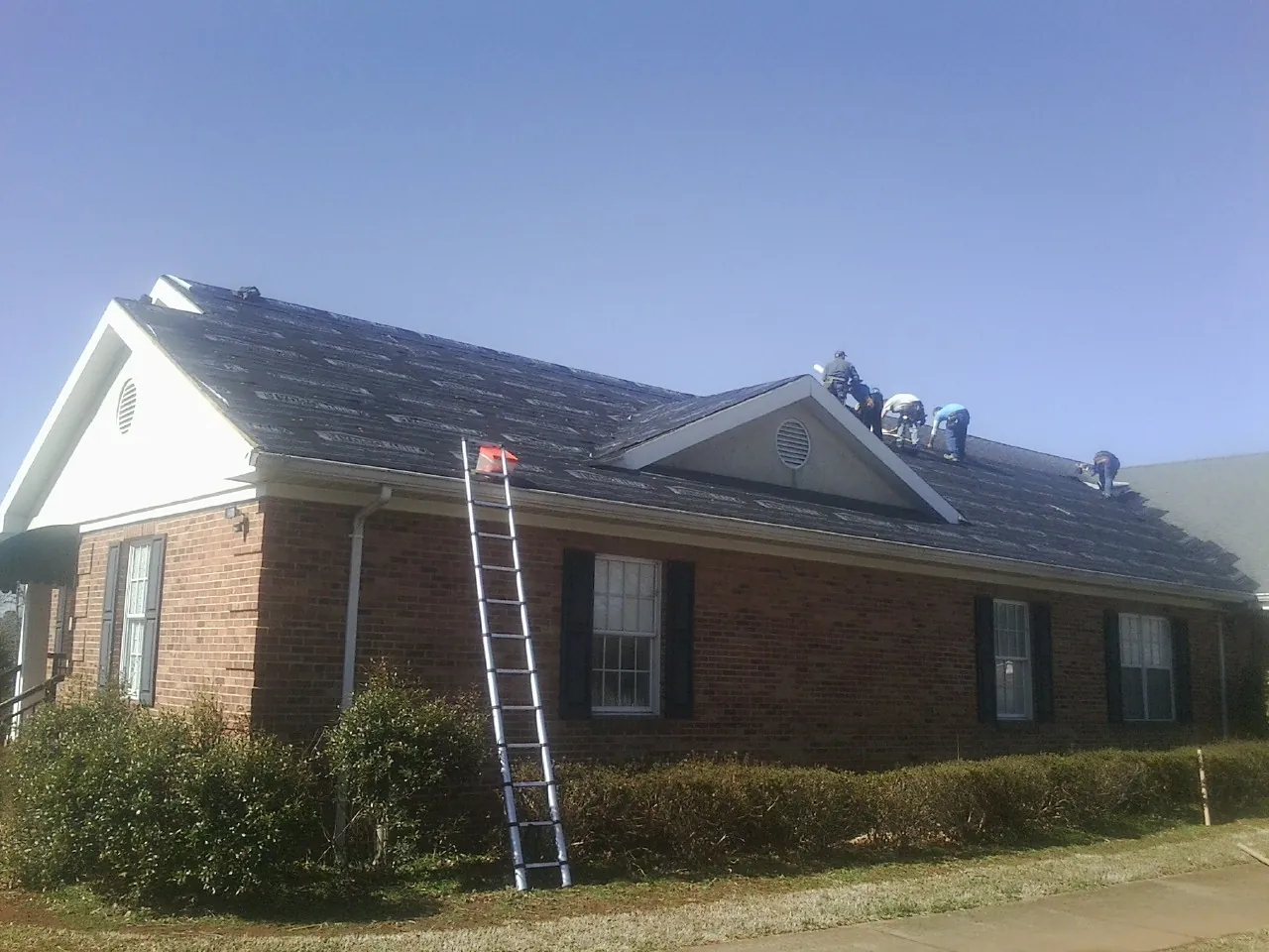 Crew tearing shingles off a brick ranch roof with a ladder set — Metal Roof Repair work by our crew in Fleetwood