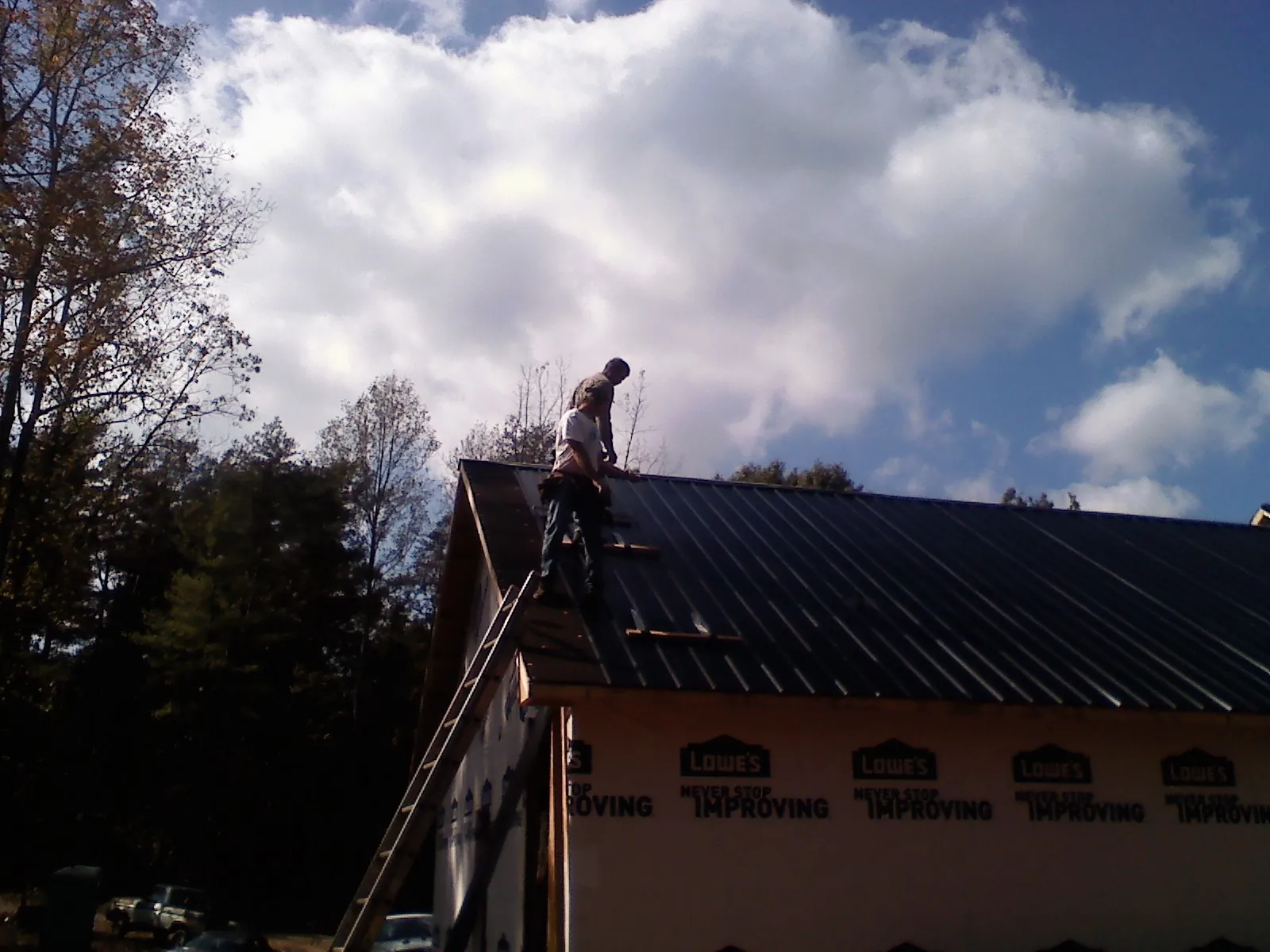 Roofer fastening dark metal panels high against a cloudy sky, from a Roof Inspection job in Fleetwood